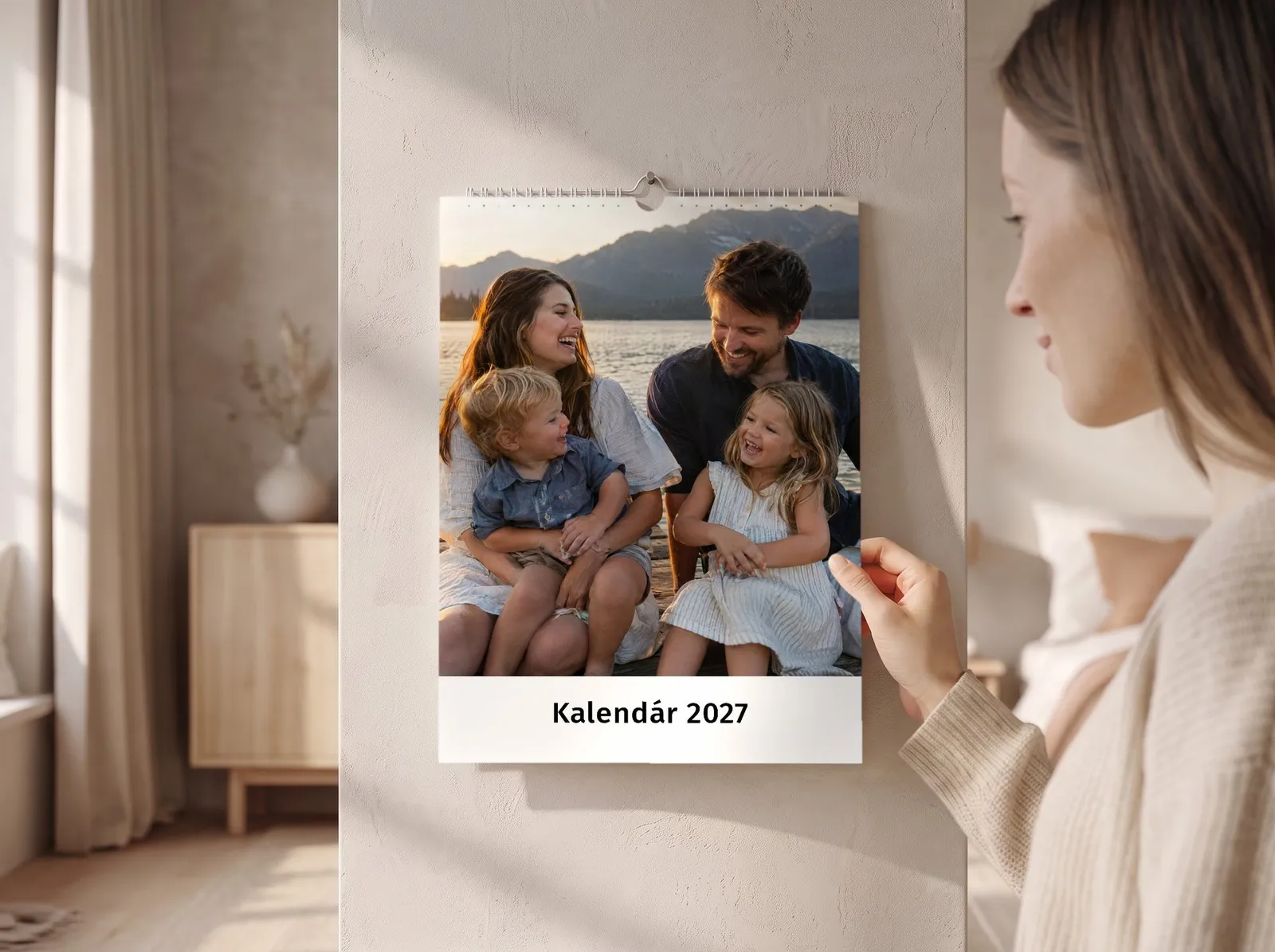 Žena si prezerá nástenný fotokalendár na stene svetlej spálne, na liste rodina pri jazere v horách